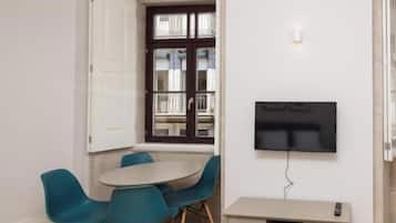 Un espacio habitable compacto con comedor, televisor montado en la pared y un mueble auxiliar.