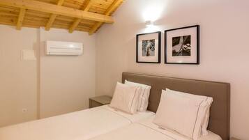 Un dormitorio con techo de madera, una cama con ropa blanca, dos cuadros en la pared y un aire acondicionado.