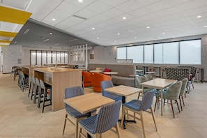 Un café moderno con zona de bar, diferentes disposiciones de asientos y amplios ventanales.