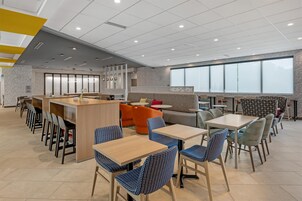 Un café moderno con zona de bar, diferentes disposiciones de asientos y amplios ventanales.