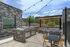 An outdoor patio with stone walls, a barbecue grill, and string lights.