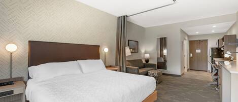 Une chambre d’hôtel avec un grand lit, un bureau, une chaise, un miroir et une kitchenette.