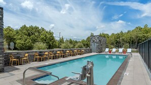 A swimming pool with a stone wall, outdoor seating, and a view of trees.