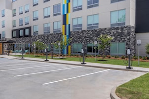 Un hotel con múltiples estaciones de carga para vehículos eléctricos, un estacionamiento y un edificio de fachada moderna.