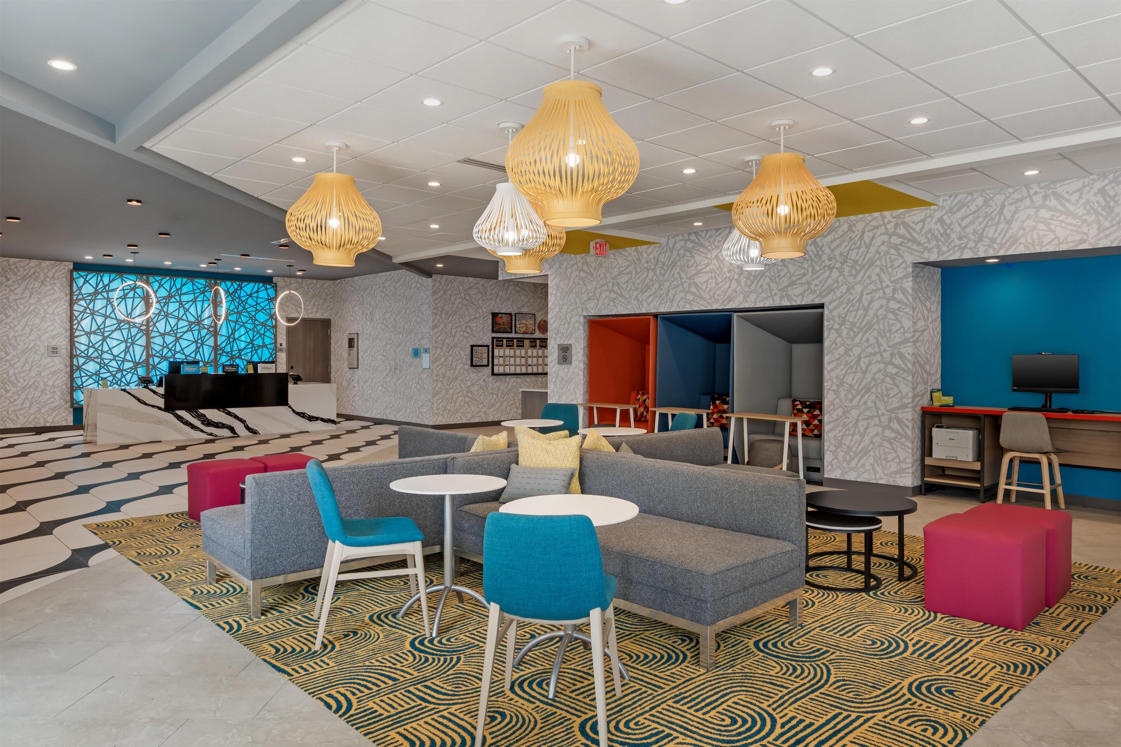 Un hall d’hôtel moderne, doté d’espaces aménagés avec des sièges, d’un comptoir de réception et d’un écran de télévision.