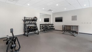 Un gimnasio con equipo de ejercicio, un televisor instalado en la pared y un tablón de anuncios con normas.