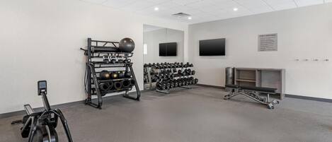 A gym with exercise equipment, a wall-mounted TV, and a bulletin board with rules.