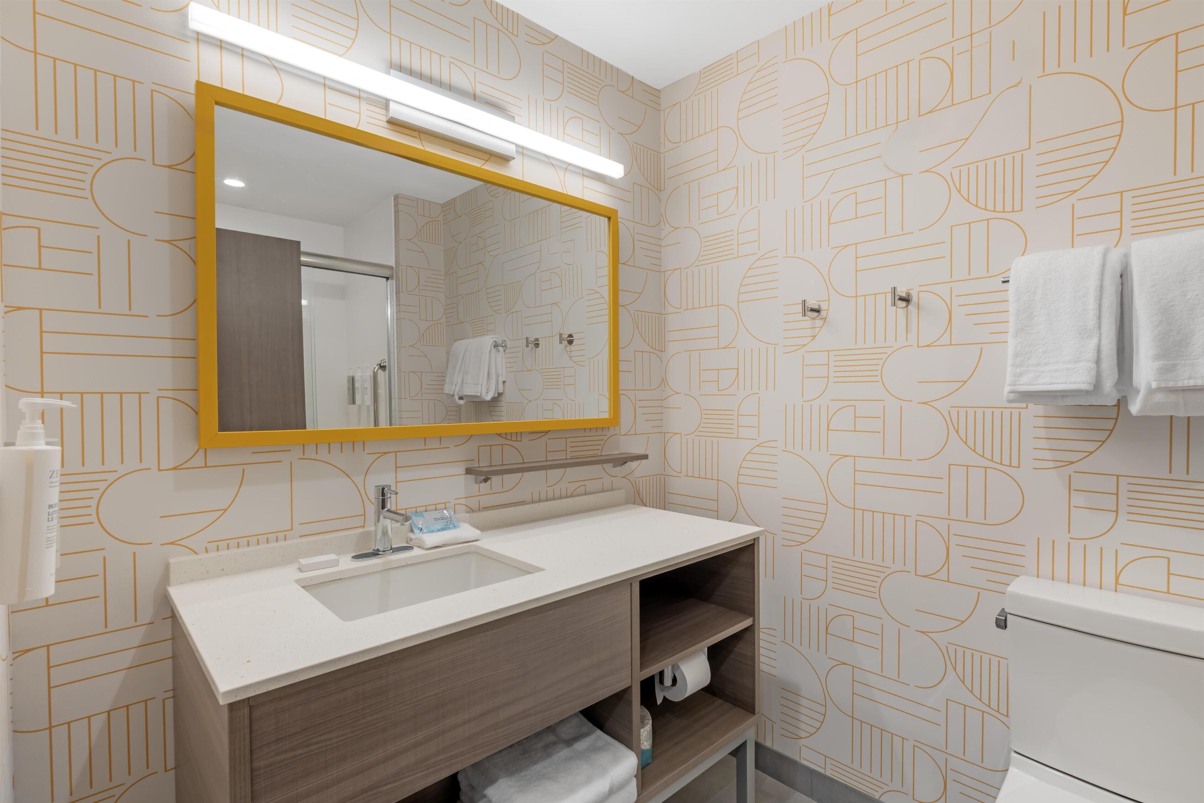 A bathroom with a white sink, a mirror with a yellow frame, and patterned wallpaper.