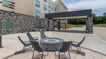 An outdoor patio with a round table and chairs, a stone wall, and a covered seating area.