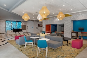 A modern hotel lobby with seating areas, a reception desk, and a TV screen.