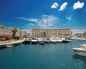 A marina with boats docked, a large building in the background, and a clear blue sky.