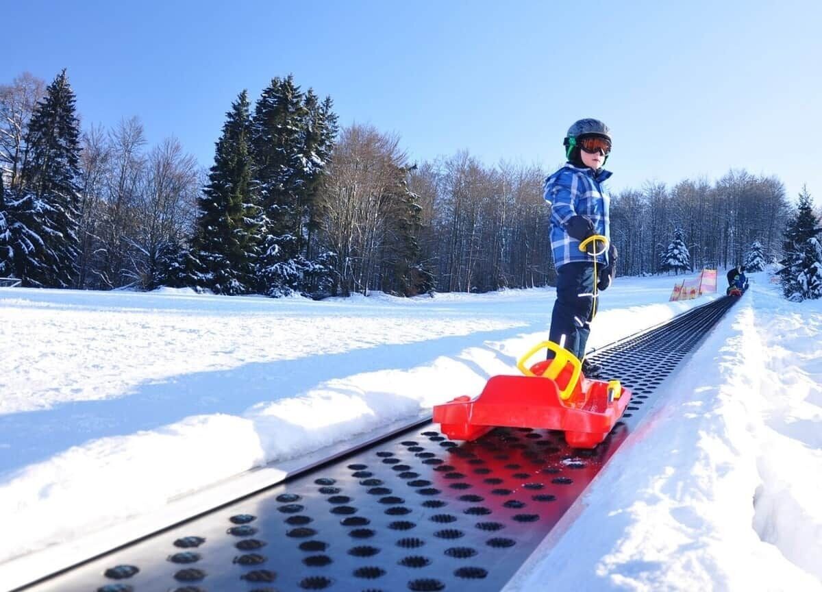 Une personne se tient sur une voie ferrée en métal, avec de la neige de chaque côté, et est entourée d’arbres.