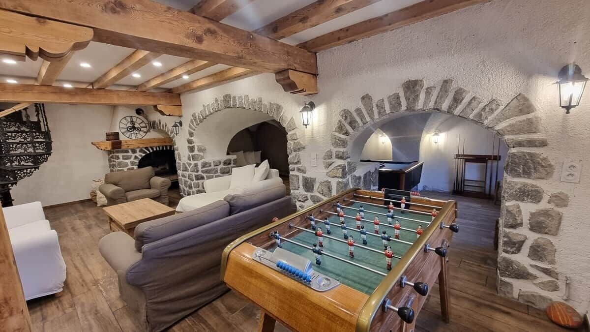 Um quarto acolhedor com mesa de futebol, paredes de pedra, vigas de madeira e lareira.