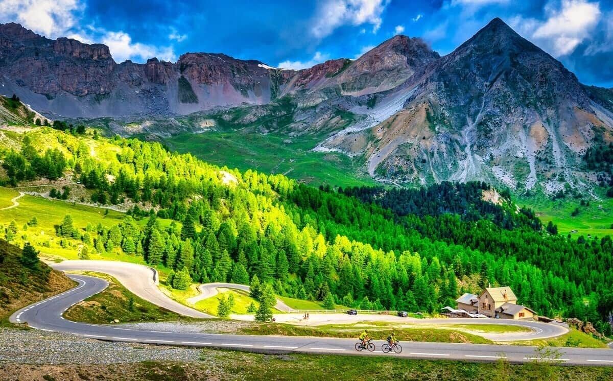 A mountain landscape with a winding road and a cyclist.