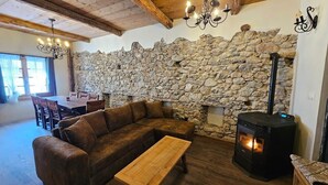 Een gezellige woonkamer met een stenen muur, een bank, een houten tafel en een houtkachel.