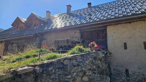 A rustic building with a stone wall, wooden benches, and potted plants.