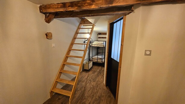 Een smalle gang met een houten ladder naar een slaapkamer met stapelbedden.