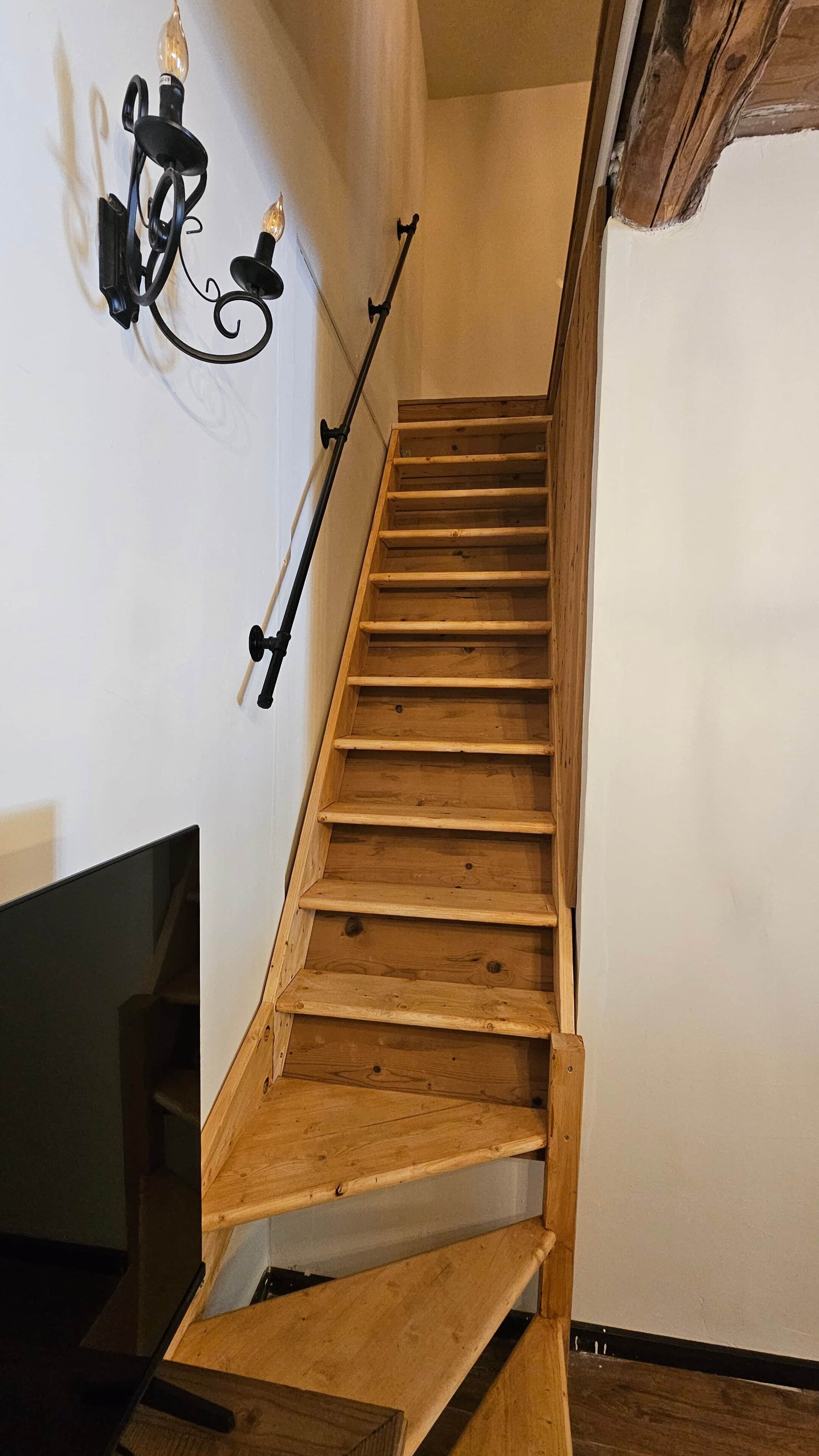 A wooden staircase with a handrail, a wall-mounted light fixture, and a wooden door at the bottom.