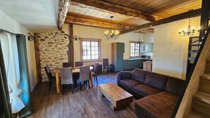 Un intérieur rustique avec un mur en pierre, un plafond en bois, un coin repas avec des chaises et une table, un canapé et un escalier.