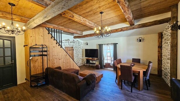 Un intérieur rustique avec des poutres apparentes, un escalier, un canapé, une table à manger et un téléviseur.