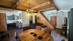 Un intérieur rustique avec une table à manger en bois, des sièges en cuir, un lustre, une cuisine et un escalier en pierre.