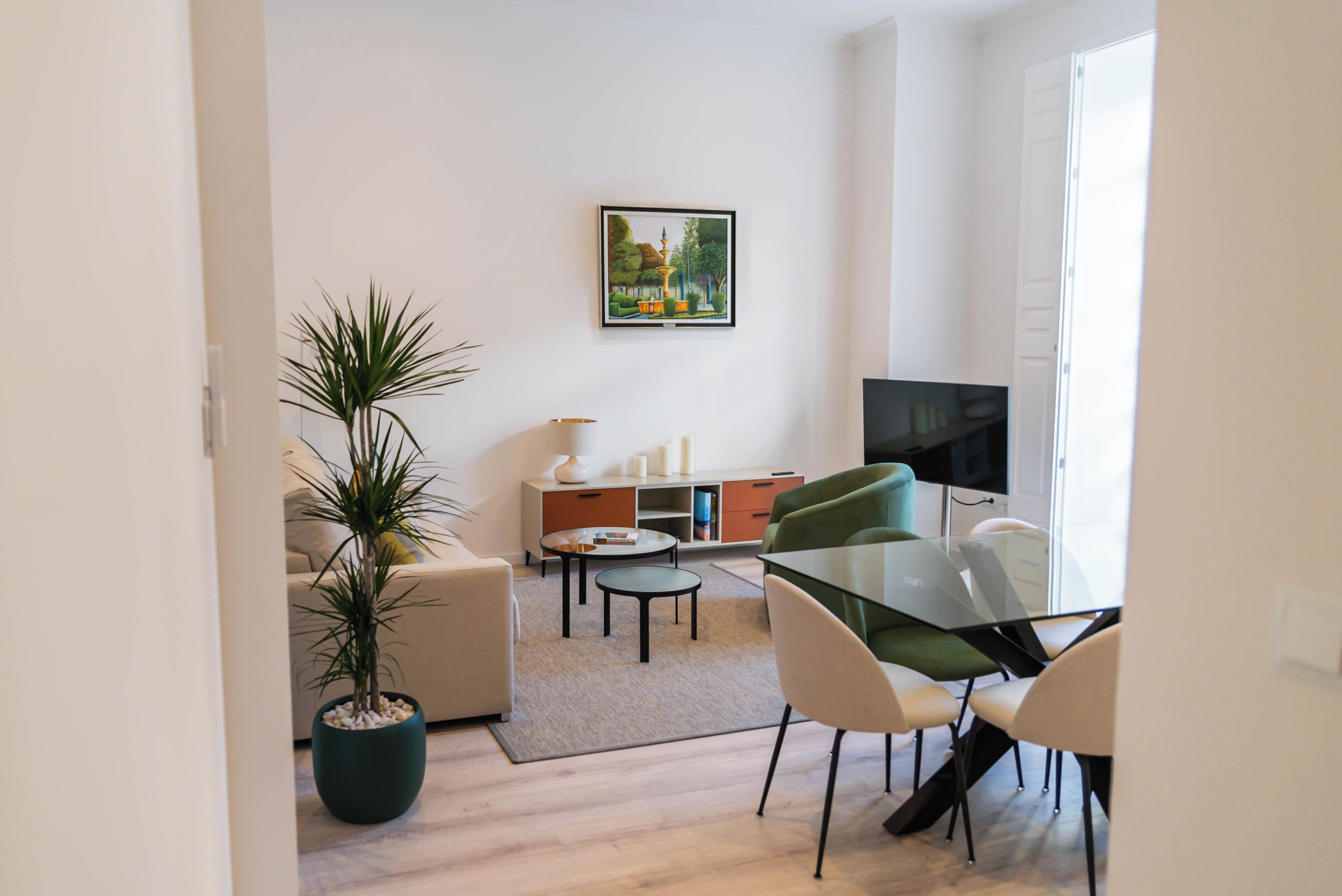 Un salon moderne avec un canapé, une table à manger et des chaises, un téléviseur, une plante en pot et un tableau accroché au mur.