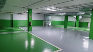 Un área de estacionamiento interior limpio y bien iluminado, con paredes y pilares verdes y blancos, y un extintor montado en un pilar.