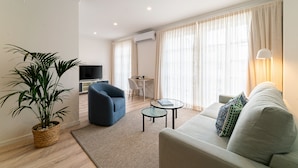 Una sala de estar moderna con sofá, sillón, televisor y una planta en maceta.