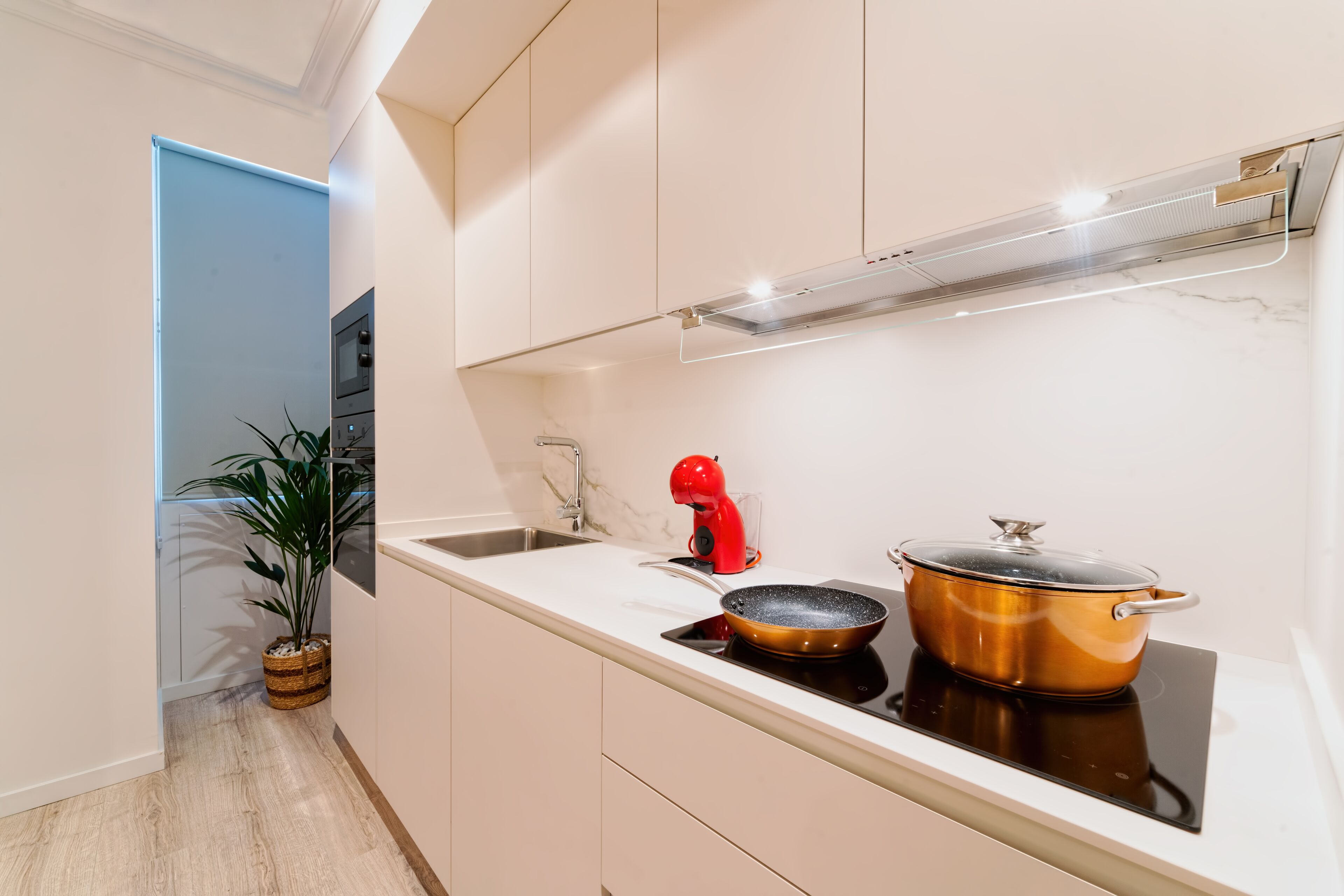 Una cocina moderna con estufa integrada, un lavamanos y un hervidor rojo.