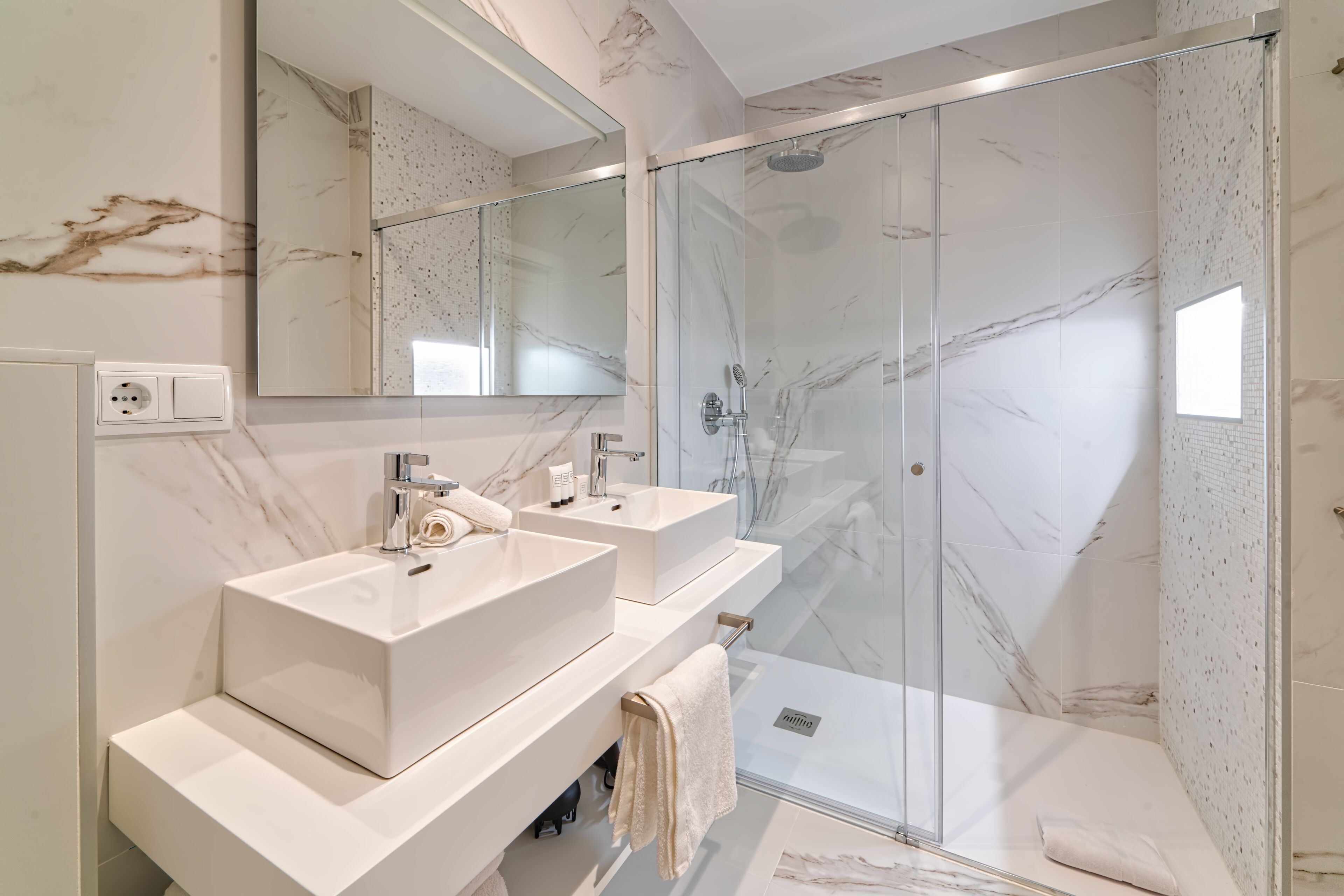 A modern bathroom with two sinks, a shower, and a large mirror.