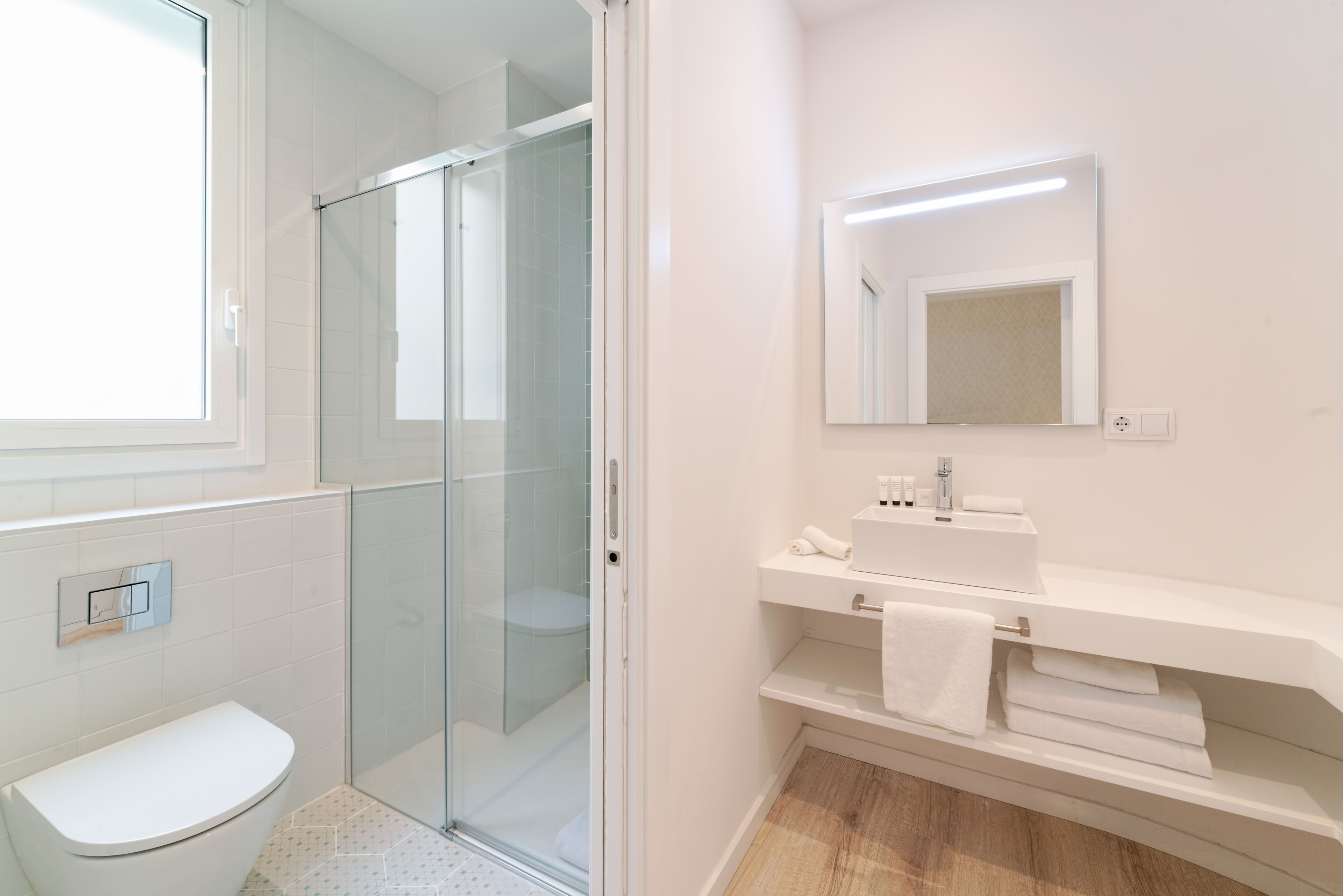 A modern bathroom with a glass shower enclosure, a white toilet, and a vanity with a mirror and towel rack.