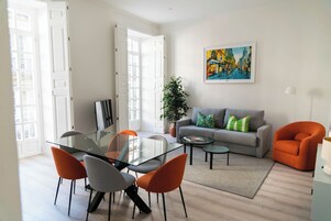 Una sala de estar moderna con una mesa de comedor de vidrio, un sofá gris, un sillón naranja y un cuadro en la pared.