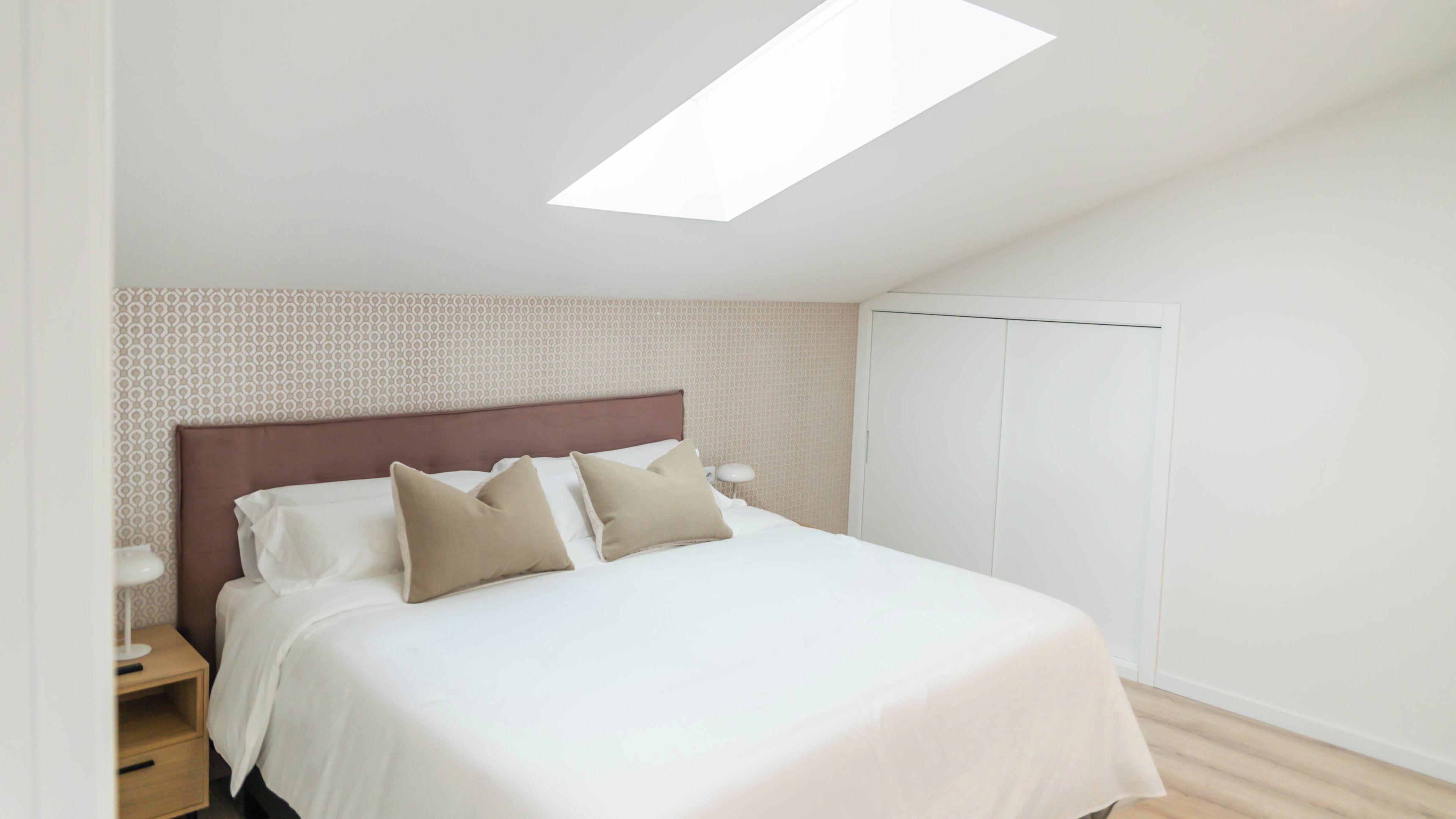 A bedroom with a bed, nightstands, a wardrobe, and a skylight.