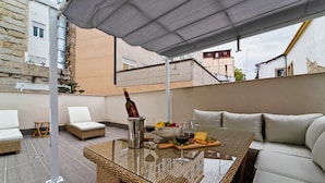 Un área de estar al aire libre con una mesa de vidrio, muebles de mimbre y un sofá acolchado.