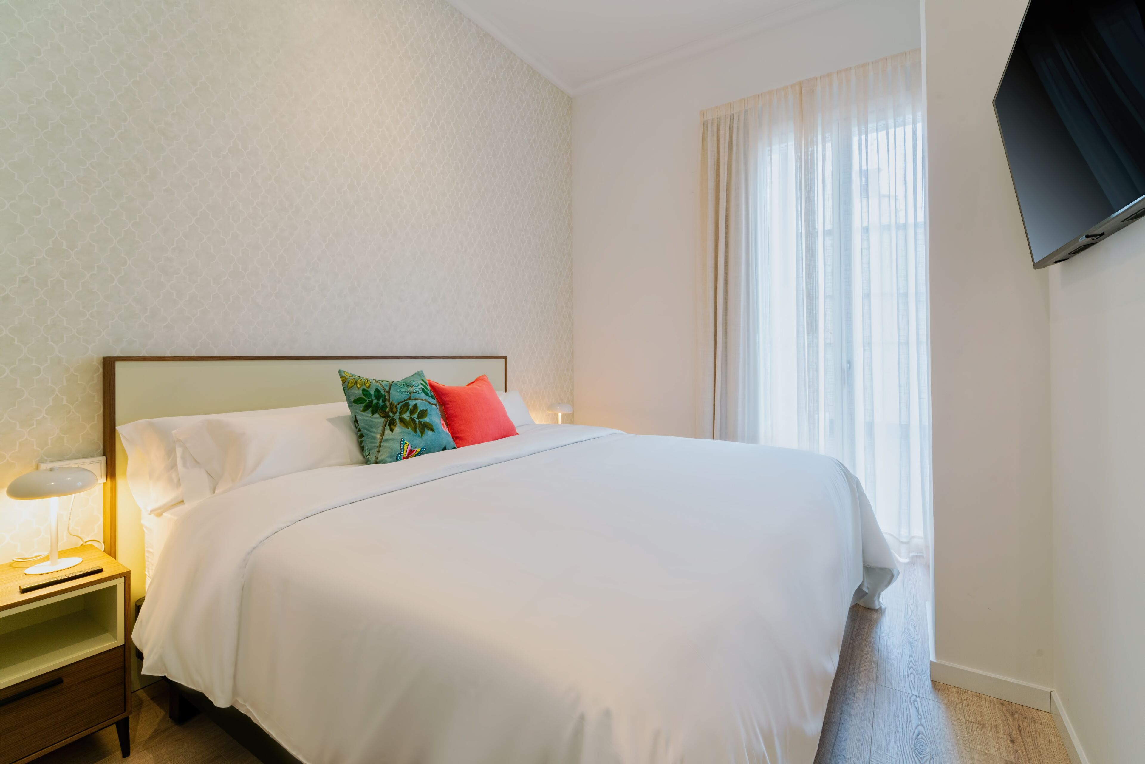 Une chambre d’hôtel équipée d’un lit, d’une table de chevet, d’une lampe et d’un téléviseur fixé au mur.