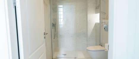 Un baño con ducha de vidrio, inodoro y suelo de mármol.