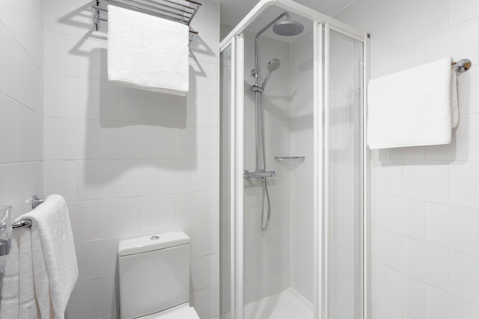 Dusche mit Glastür, Toilette und Handtuchhalter.