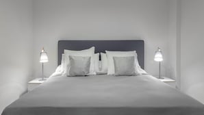 A minimalist bedroom with a large bed, two bedside lamps, and a plain wall. - Morar Apartments Malasaña (Madrid)