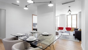 A modern dining area with a glass table, white chairs, and pendant lighting. - Morar Apartments Malasaña (Madrid)