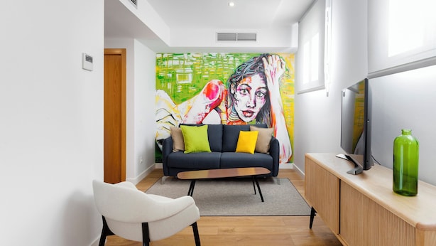 A modern living room with a sofa, a television, and a vibrant abstract painting on the wall. - Morar Apartments Malasaña (Madrid)