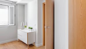 A modern, minimalistic room with a white desk, a lamp, and a potted plant. - Morar Apartments Malasaña (Madrid)