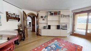 A living room with a wooden floor, a red rug, a television, and a bookshelf. - 3-room apartment with approx. (St. Moritz)