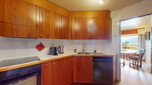 A kitchen with wooden cabinets, a coffee maker, a kettle, and a dishwasher. - 3-room apartment with approx. (St. Moritz)