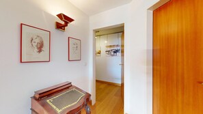 A hallway with framed artwork on the wall, a wooden door, and a piano. - 3-room apartment with approx. (St. Moritz)
