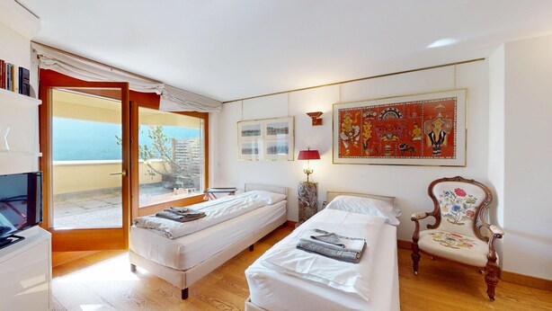 A hotel room with two beds, a desk, a chair, and a balcony with a view. - 3-room apartment with approx. (St. Moritz)