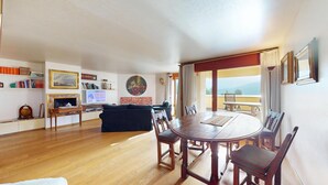 A spacious living area with a wooden dining table, comfortable seating, a television, and a balcony with a view. - 3-room apartment with approx. (St. Moritz)