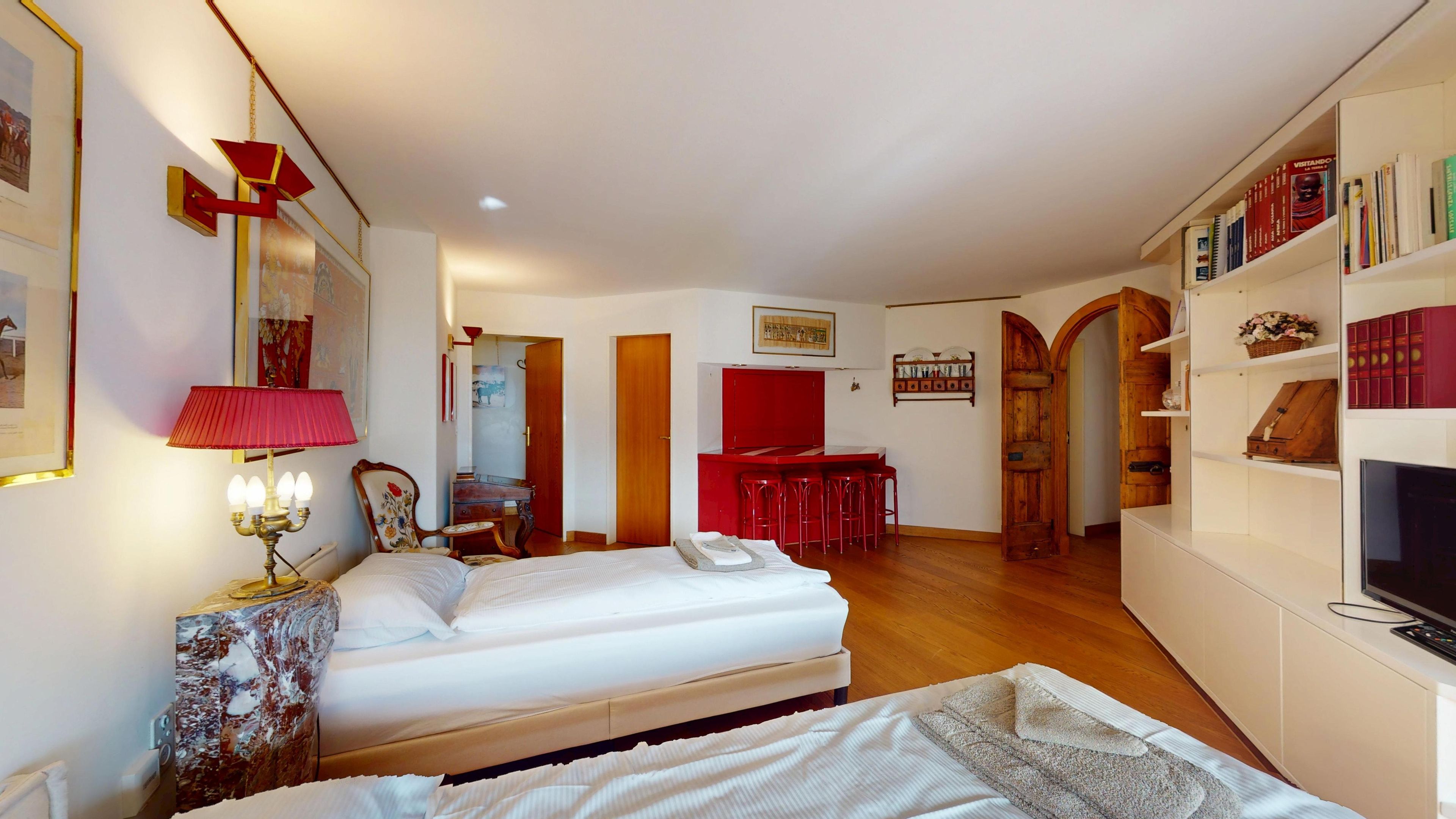 A room with two beds, a desk with chairs, a television, and a bookshelf.