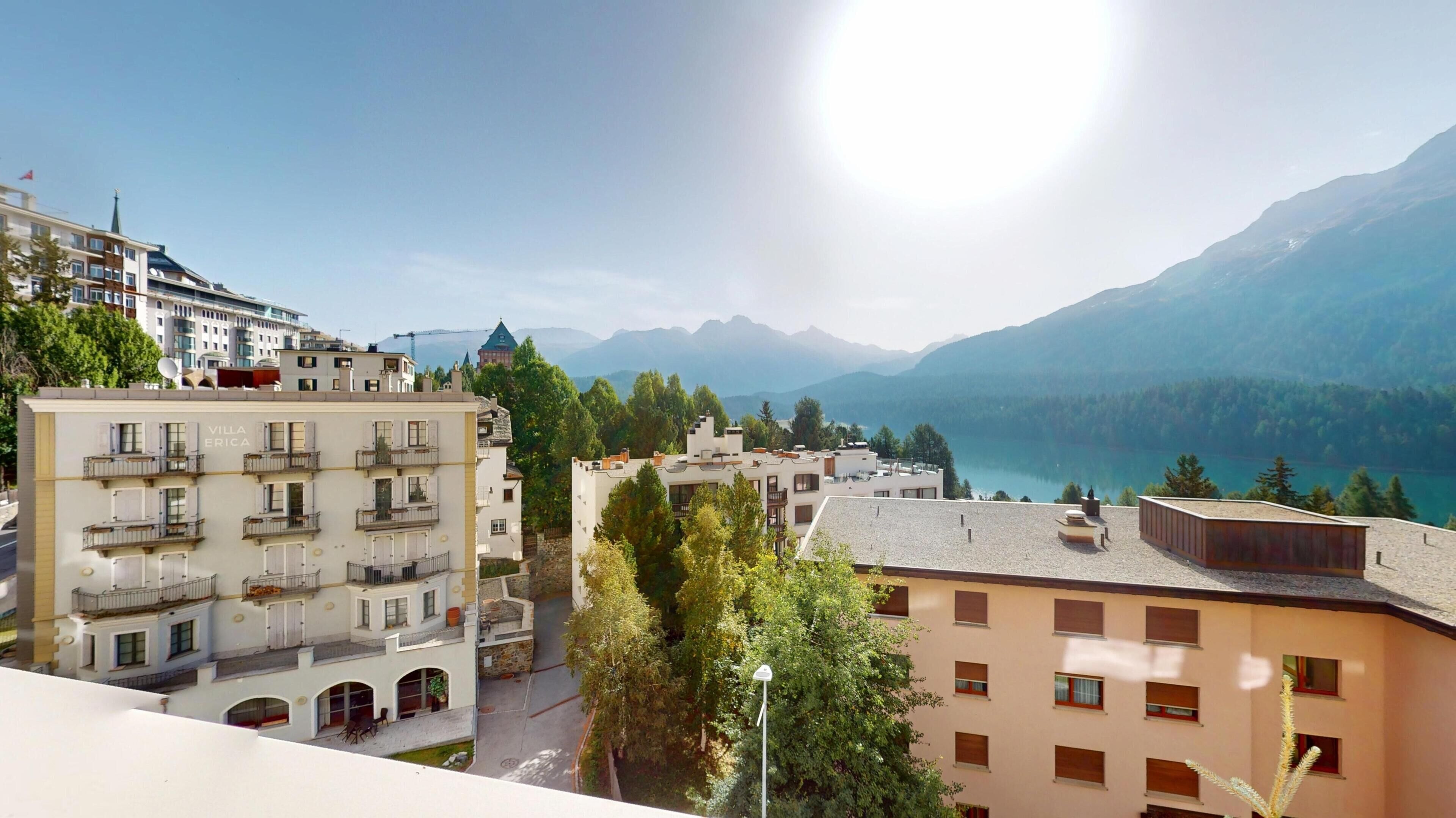 A multi-story building with balconies, a view of a lake, and mountains in the background.