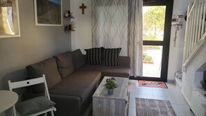 Een woonkamer met een bank, een bijzettafeltje met een plant, een kruis aan de muur en een trap naar een hoger gelegen verdieping.