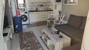 A compact living space with a sofa, a coffee table, a washing machine, a microwave, and a dining area with chairs. - Casa Zimbo in Costa Calma (Pajara)